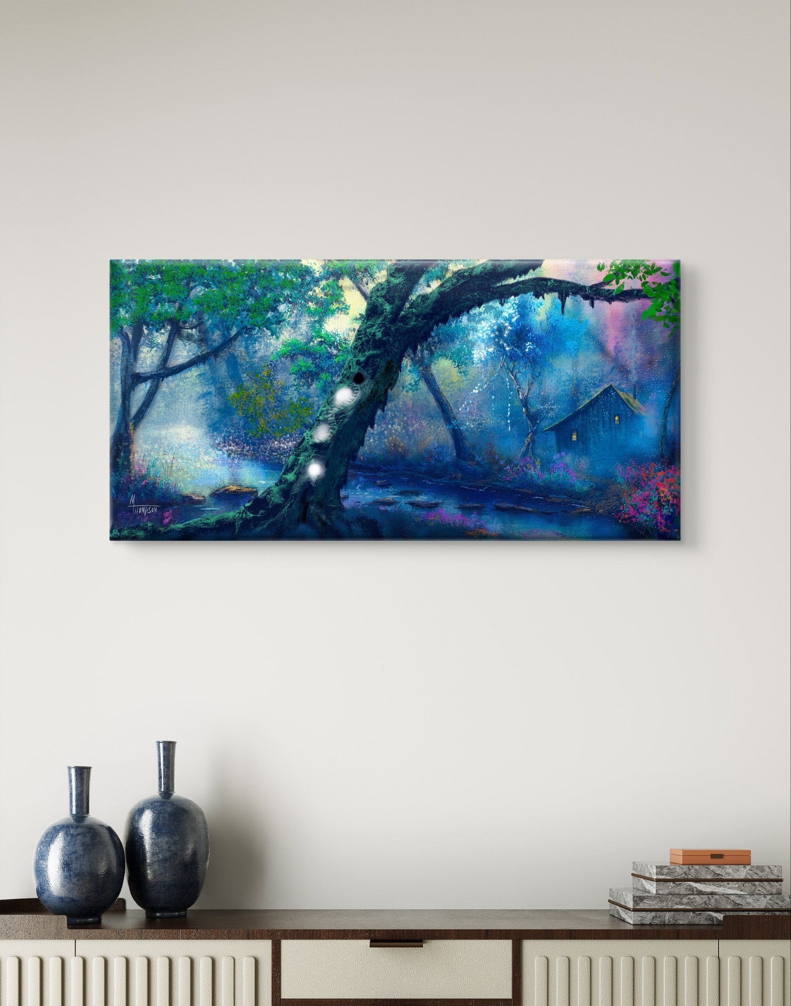Canvas print of a forest scene hanging on a wall above a wooden cabinet with decorative vases and books.