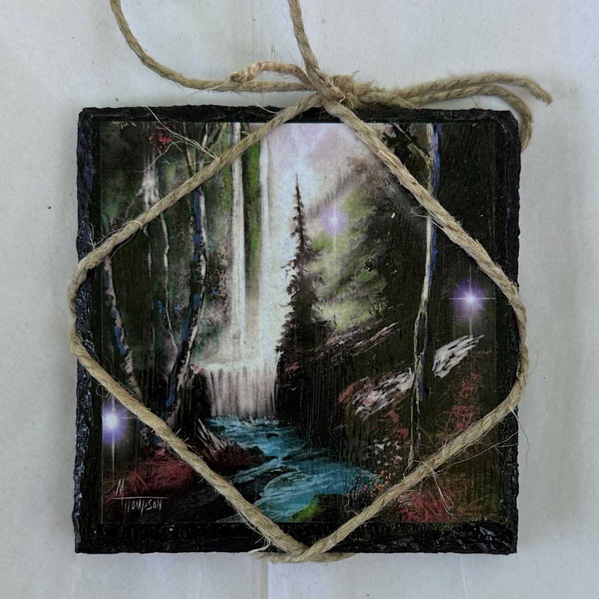 Small painting of a forest scene with a glowing light, tied with twine on a white background.