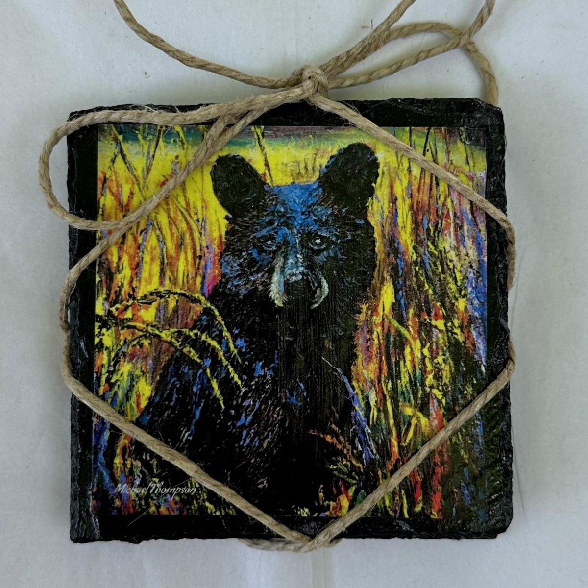 Decorative tile with a black bear design, tied with twine on a white background