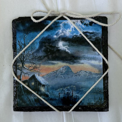 Decorative slate with a painted night scene of a house and mountains, tied with twine.