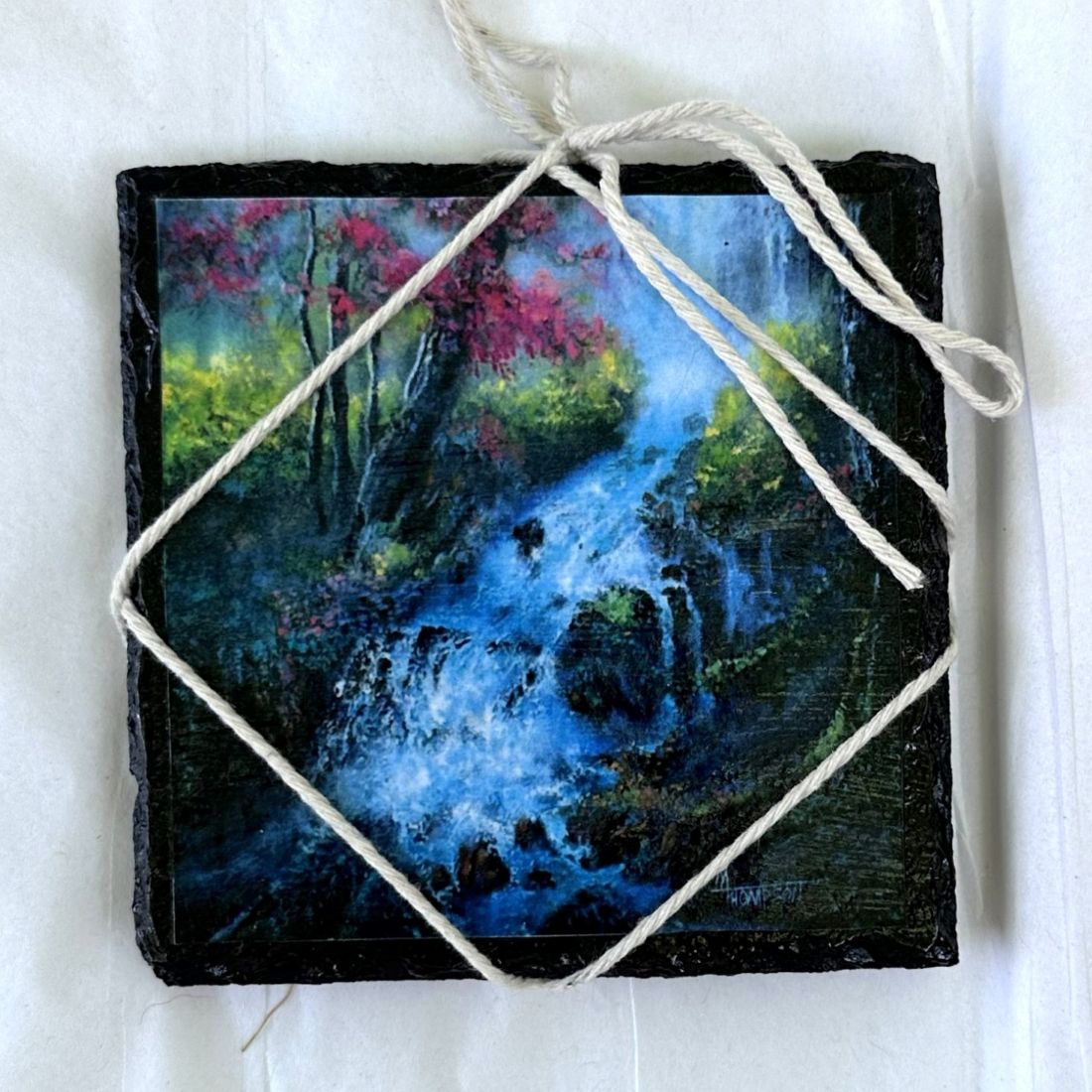 Artistic depiction of a forest scene with a stream on a small slate stone, tied with twine.