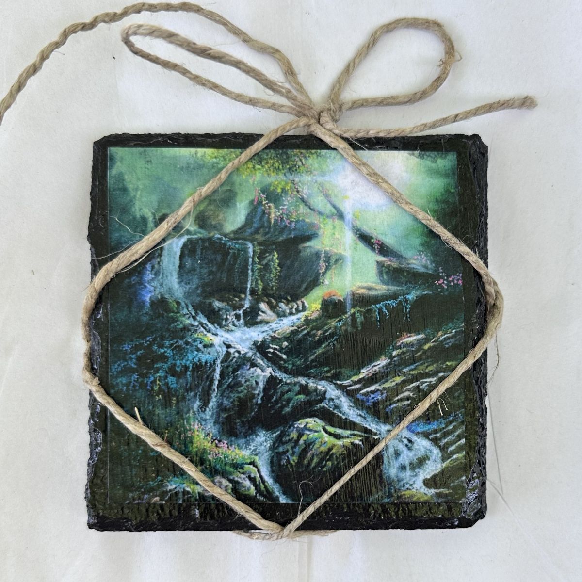 Decorative coaster with nature-themed waterfall design tied with twine on a white background                                                                                                      