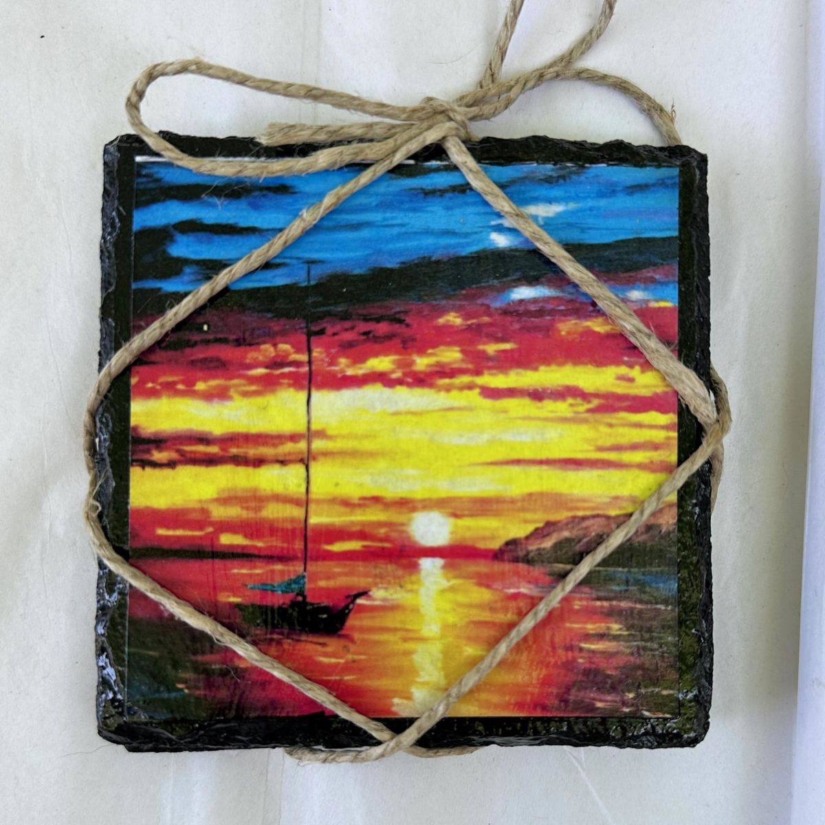 Painted slate with a sunset scene and boat, tied with twine on a white background